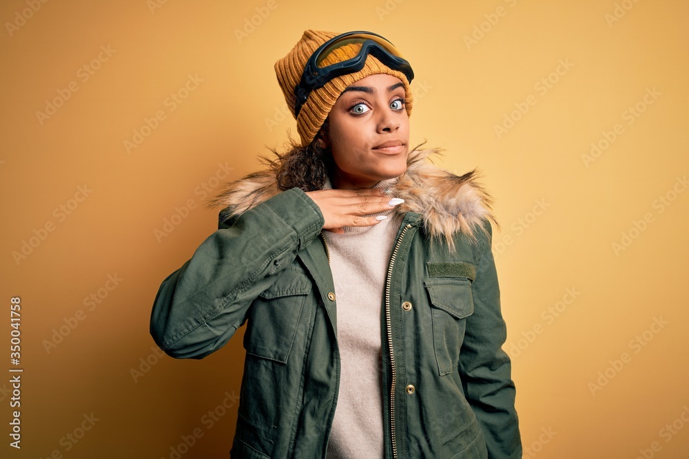 Young african american afro skier girl wearing snow sportswear and ski goggles cutting throat with hand as knife, threaten aggression with furious violence Young african american afro skier girl wearing snow sportswear and ski goggles cutting throat with hand as knife, threaten aggression with furious violence