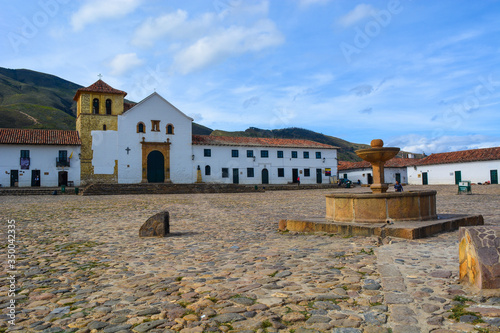 "Plaza Mayor" of Villa de Leyva, Boyacá with blue sky and cobbled paths with the Our Lady of Rosario Church or Cathedral in the background, and the fountain of the town in the middle.