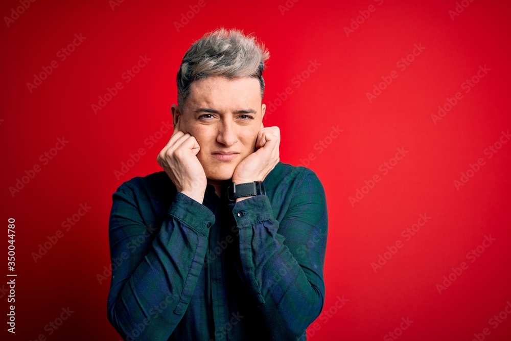 Young handsome modern man wearing elegant green shirt over red isolated background covering ears with fingers with annoyed expression for the noise of loud music. Deaf concept. Young handsome modern man wearing elegant green shirt over red isolated background covering ears with fingers with annoyed expression for the noise of loud music. Deaf concept.