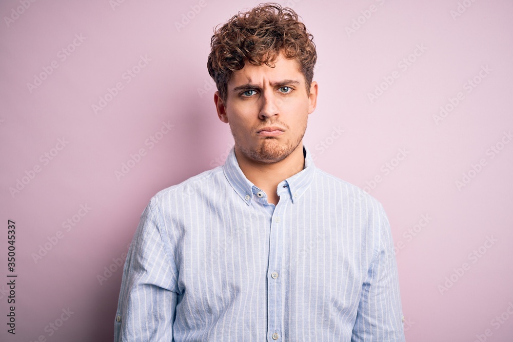 Young blond handsome man with curly hair wearing striped shirt over white background depressed and worry for distress, crying angry and afraid. Sad expression. Young blond handsome man with curly hair wearing striped shirt over white background depressed and worry for distress, crying angry and afraid. Sad expression.