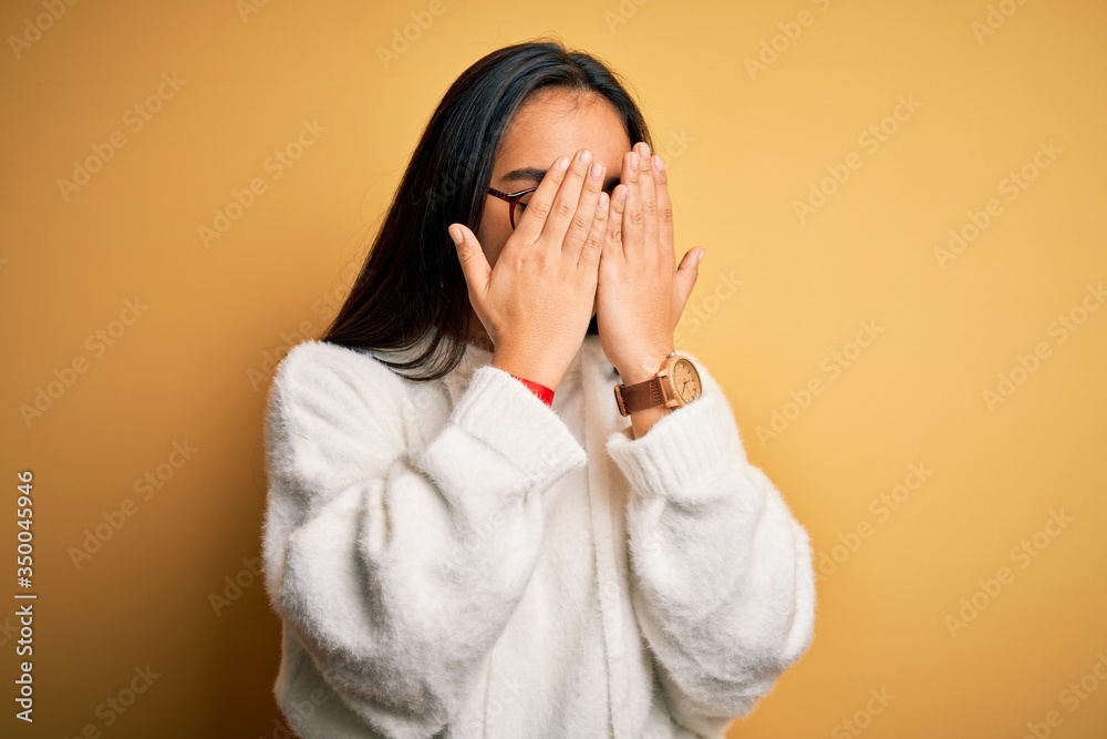 Young beautiful asian woman wearing casual sweater and glasses over yellow background with sad expression covering face with hands while crying. Depression concept. Young beautiful asian woman wearing casual sweater and glasses over yellow background with sad expression covering face with hands while crying. Depression concept.