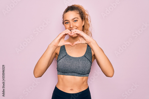 Young beautiful blonde sportswoman with blue eyes doing exercise wearing sportswear smiling in love doing heart symbol shape with hands. Romantic concept.