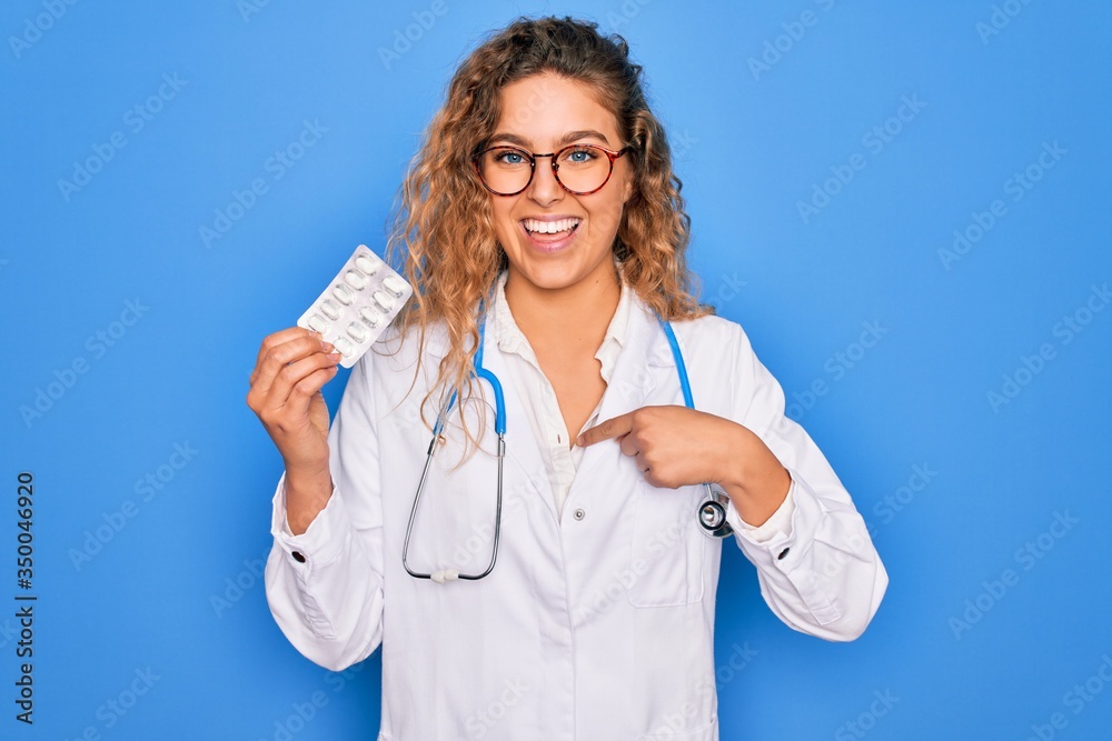 Young beautiful blonde doctor woman with blue eyes wearing stethoscope holding pills with surprise face pointing finger to himself Young beautiful blonde doctor woman with blue eyes wearing stethoscope holding pills with surprise face pointing finger to himself