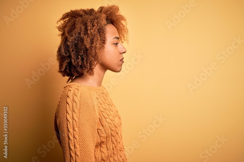 Young beautiful African American afro woman with curly hair wearing casual sweater looking to side, relax profile pose with natural face with confident smile.