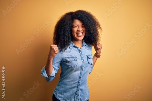 Young beautiful african american woman with afro hair standing over yellow isolated background excited for success with arms raised and eyes closed celebrating victory smiling. Winner concept.