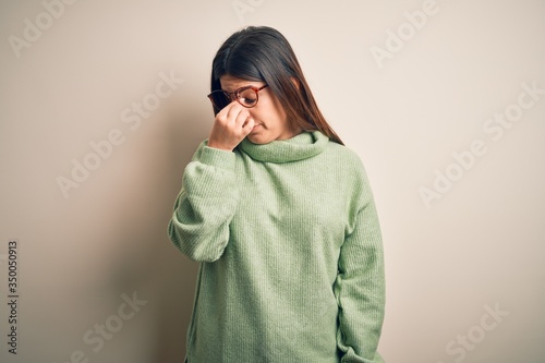 Young beautiful woman wearing casual sweater standing over isolated white background tired rubbing nose and eyes feeling fatigue and headache. Stress and frustration concept. © Krakenimages.com