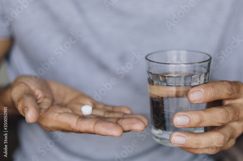 Sick man with a glass of water and pills, Taking medication to alleviate illness