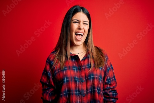 Young beautiful woman wearing casual shirt over red background winking looking at the camera with sexy expression, cheerful and happy face. © Krakenimages.com