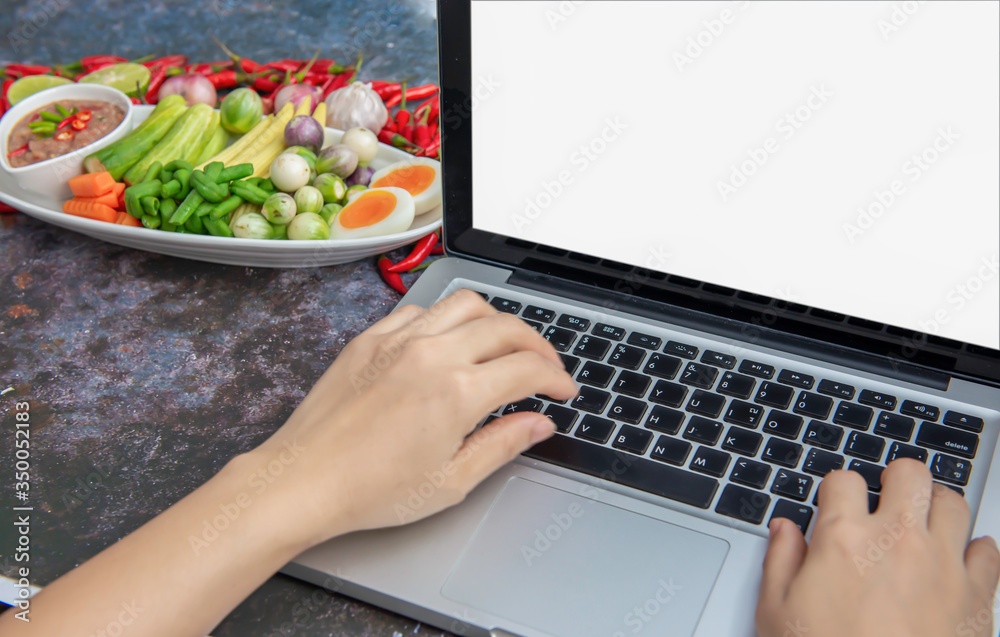Hand on Laptop isolated white screen over beautiful food, Chilli shrimp paste with fresh vegetable on wood table, to share on social media, social market.