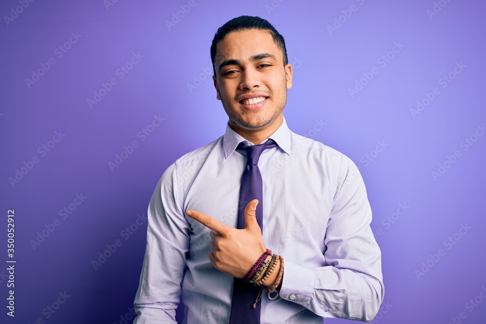 Young brazilian businessman wearing elegant tie standing over isolated purple background cheerful with a smile on face pointing with hand and finger up to the side with happy and natural expression Young brazilian businessman wearing elegant tie standing over isolated purple background cheerful with a smile on face pointing with hand and finger up to the side with happy and natural expression