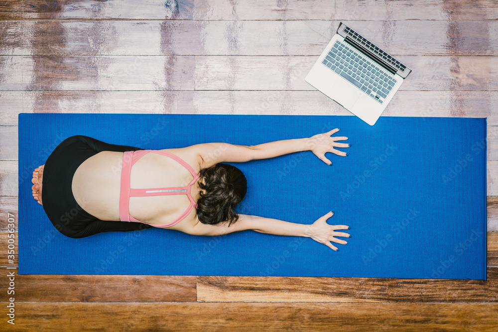 Top view Asian woman practicing yoga from home with laptop when Covid19 outbreak