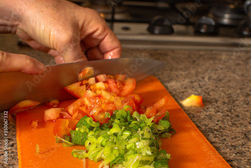 Woman hand cutting red raw tomatoes over orange cutting board