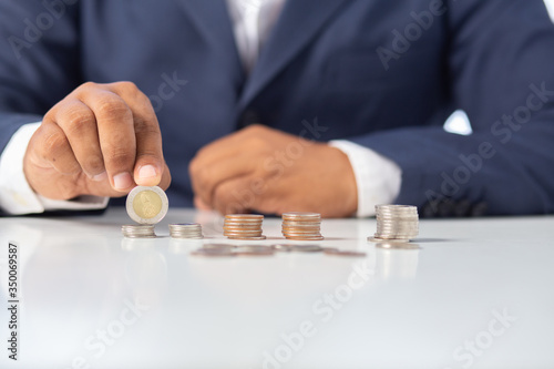 Businessman hand with putting money coins in the office concept: Saving money wealth and financial Personal, finance management loan for a home, diagram chart earnings to plan profit