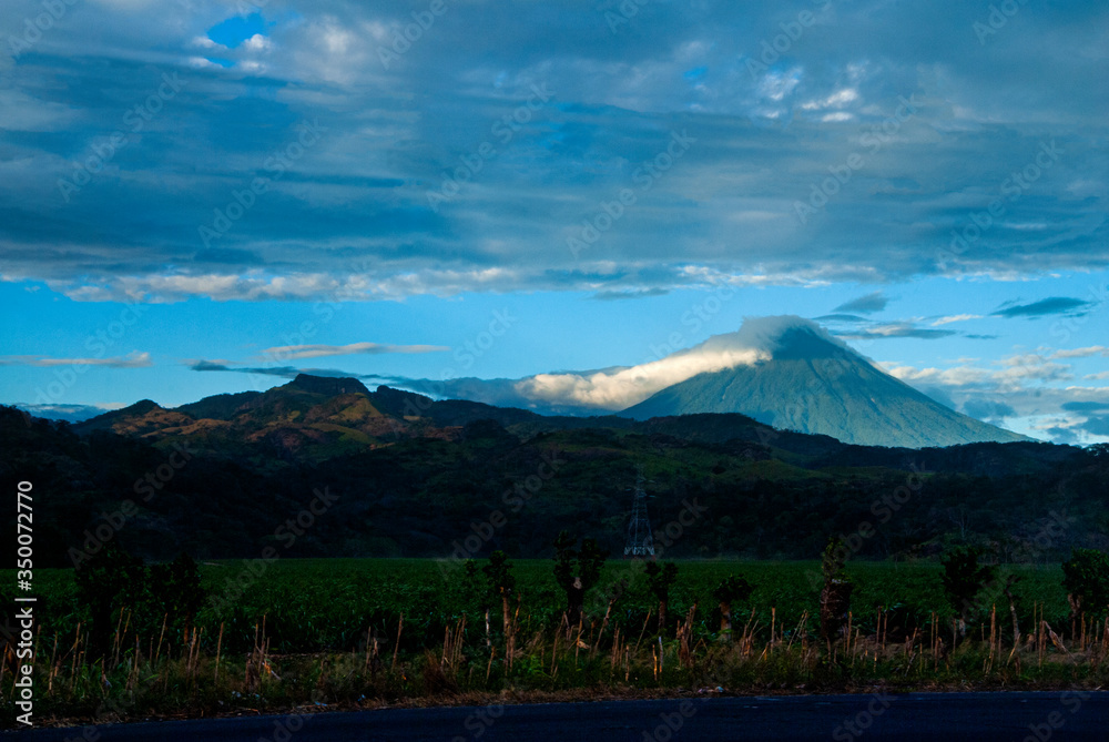 Fototapeta premium Volcano covered with clouds in Guatemala, forest landscape at imposing sunset on the horizon.