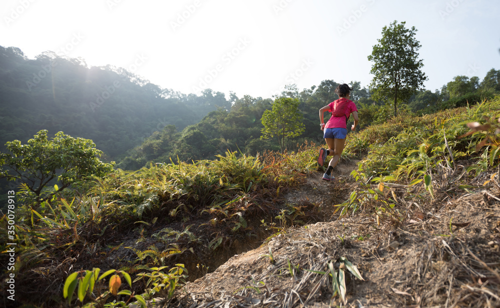 Woman trail runner running up on mountain slope in tropical forest