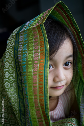 Portrait of cute Asian toddler, kid, girl during Hair Raya, Eid Mubarak celebration in Malaysia. Wearing traditional songket shawl. photo