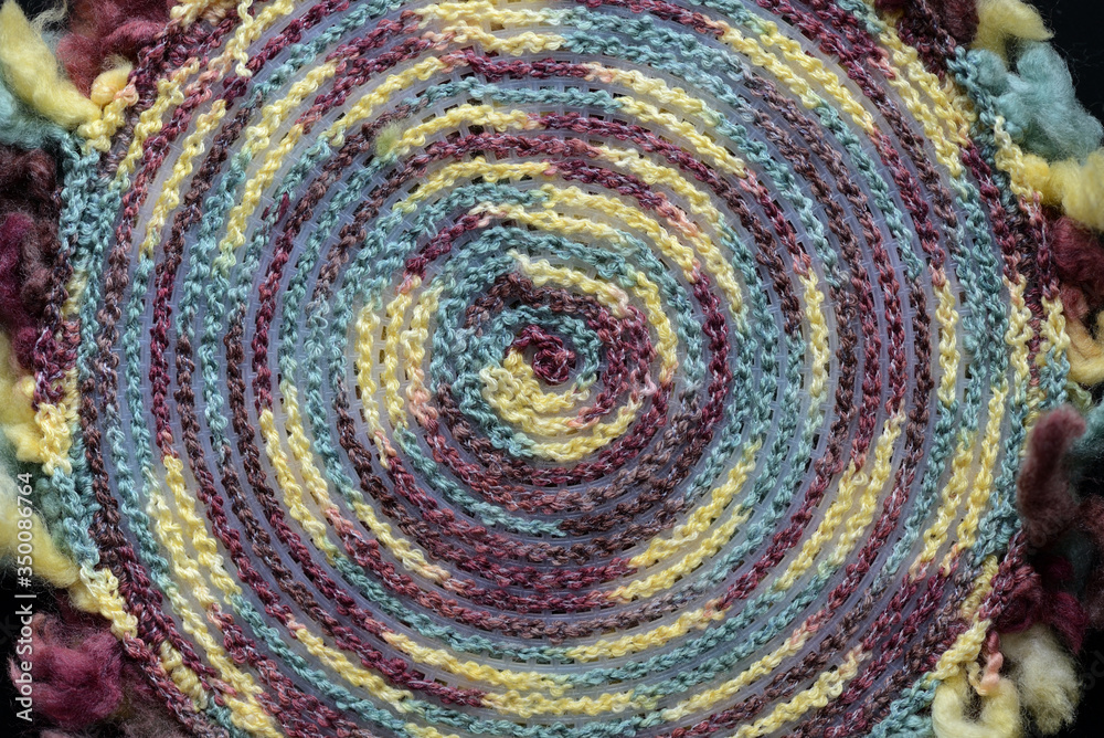 Fragment of a crocheted circle from melange threads based on a plastic canvas from the wrong side on a black background close-up