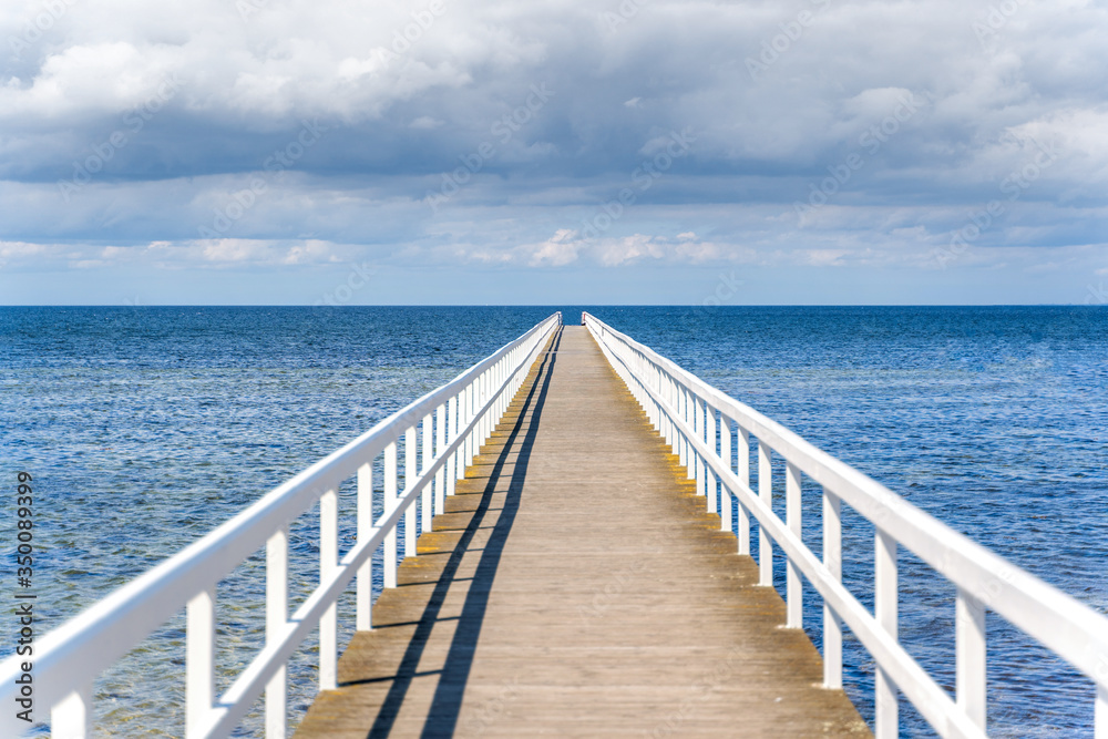 Wooden white bridge to the sea with dramatic sky view over the long jetty.