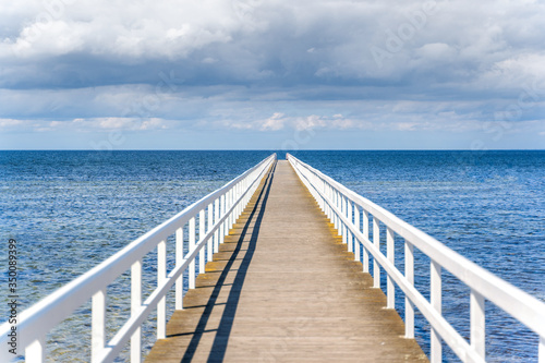 Wooden white bridge to the sea with dramatic sky view over the long jetty.