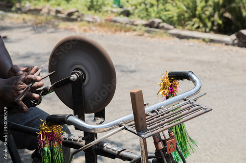 an indian man sharpening a steel scissor on rotating whetstone photo