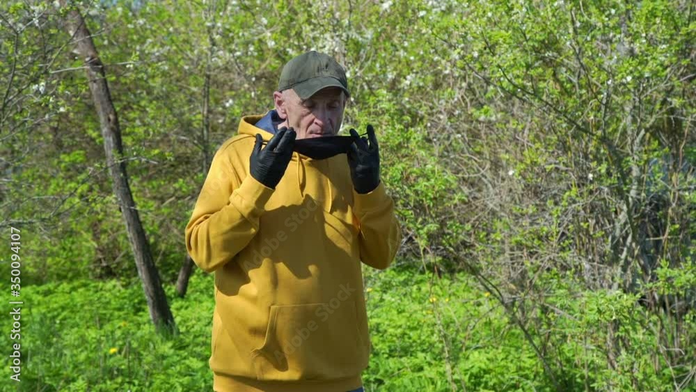 old man in sterile gloves puts black disposable mask on standing among green trees on sunny spring day slow motion old man in sterile gloves puts black disposable mask on standing among green trees on sunny spring day slow motion