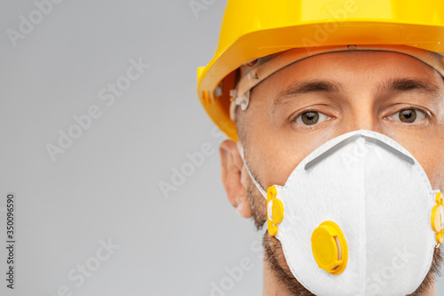 profession, construction and building - male worker or builder in helmet and respirator mask over grey background