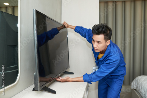 Vietnamese service worker installing television set in apartment of client