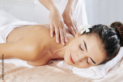 Smiling young woman enjoying relaxing neck and back massage in spa salon