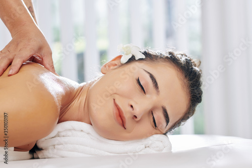 Pretty young woman smiling with pleasire when receiving relaxing back massage in spa salon