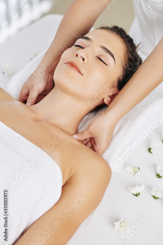 Smiling young woman enjoying relaxing shoulder massage in spa salon