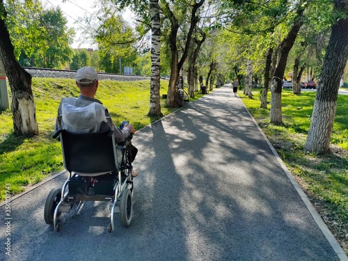 an unrecognizable disabled man in a wheelchair Park. a lone disabled person in an electric wheelchair moves along an empty summer alley.