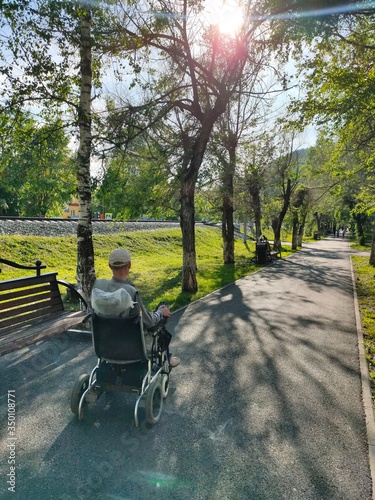an unrecognizable disabled man in a wheelchair Park. a lone disabled person in an electric wheelchair moves along an empty summer alley.