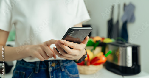 Woman hand holding smartphone at home in kitchen.