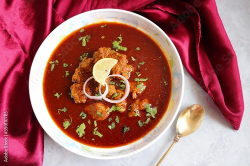 Indian Food- Kolhapuri Mutton tambda rassa or red meat curry is authentic Kolhapur’s very spicy lamb gravy dish. Cooked with Indian spices & garnished with coriander, onion & lemon wedge. Copy space. photo