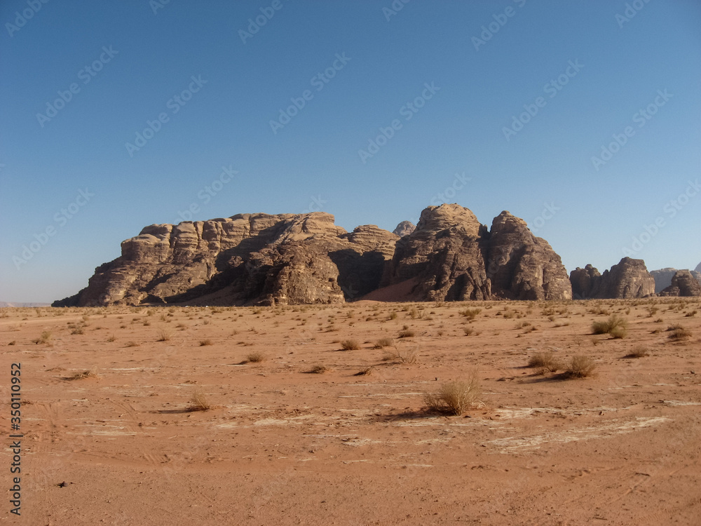Early morning in the Arabian desert. The tracks from the car's tires go in the direction of the silhouettes of mountains on the horizon. Early morning in the Arabian desert. The tracks from the car's tires go in the direction of the silhouettes of mountains on the horizon.