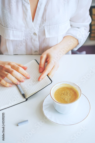 girl makes notes in a notebook, next is a coffee mug