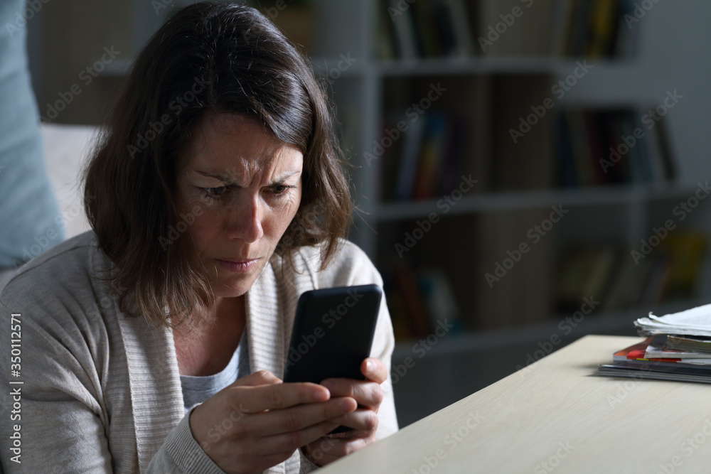 Worried adult woman reading news on phone at night at home