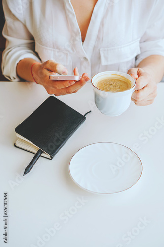 girl in a black jacket holds a phone and a mug of coffee in her hand