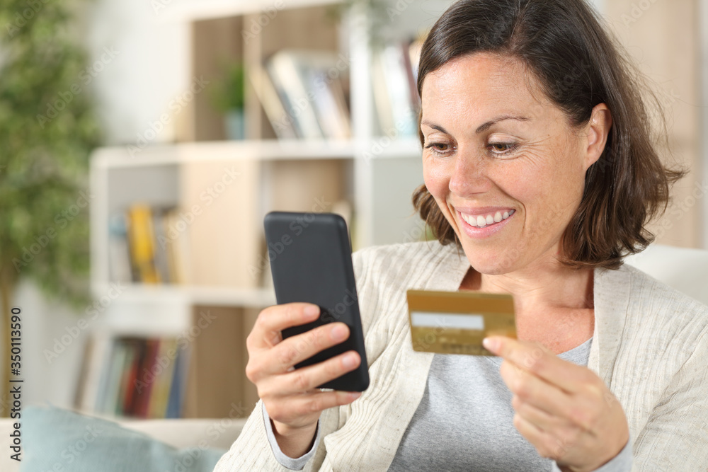 Happy adult woman paying with card on phone at home Happy adult woman paying with card on phone at home