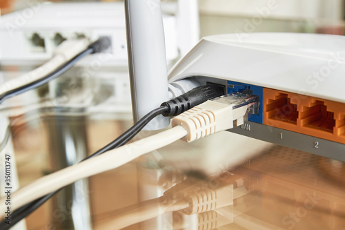 Two white wireless routers on a glass table connected by cables to the Internet. Close-up