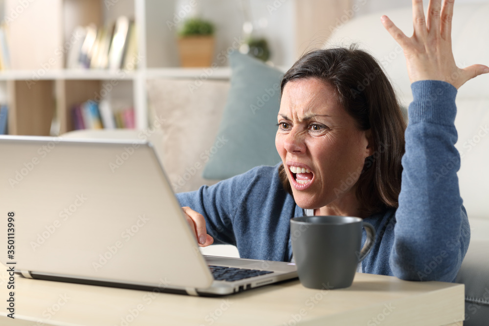 Angry adult woman watching video on laptop at home