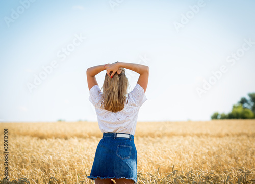 Blonde caucasian and happy girl in a white blouse and blue denim skirt in a wheat field enjoys freedom. Concept people in harmony with nature. Female psychology, feelings and emotions.