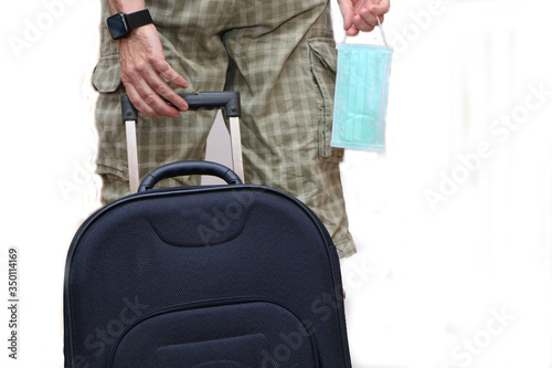 A man pulls a suitcase from the back and holds a medical mask in his hand.