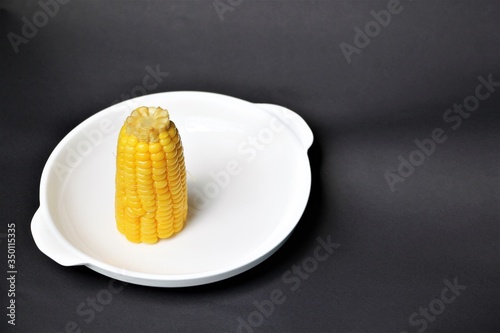 Corn on a white plate, a black background, Corn is a valuable plant that is a staple of Westerners, valuable in vitamin A, vitamin B, minerals, dietary fiber and as a source of antioxidants. photo