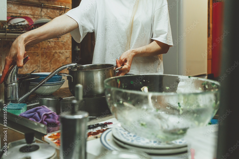 Unrecognizable woman washes dishes in kitchen