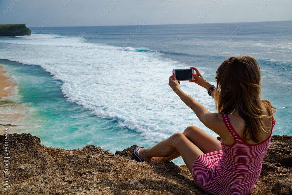 Woman tourist takign photos with her smartphone at a vacation on tropical island.