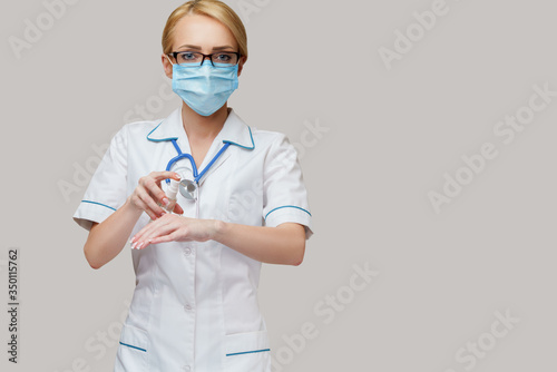 Φωτογραφία medical doctor nurse wearing protective mask - holding bottle of sanitizing spra
