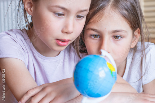 Child girl are sitting at home and looking at the globe, dreaming about traveling around the world.