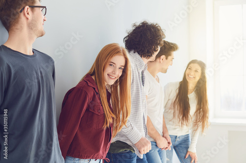 A group of smiling friends is standing in a bright room with a window.