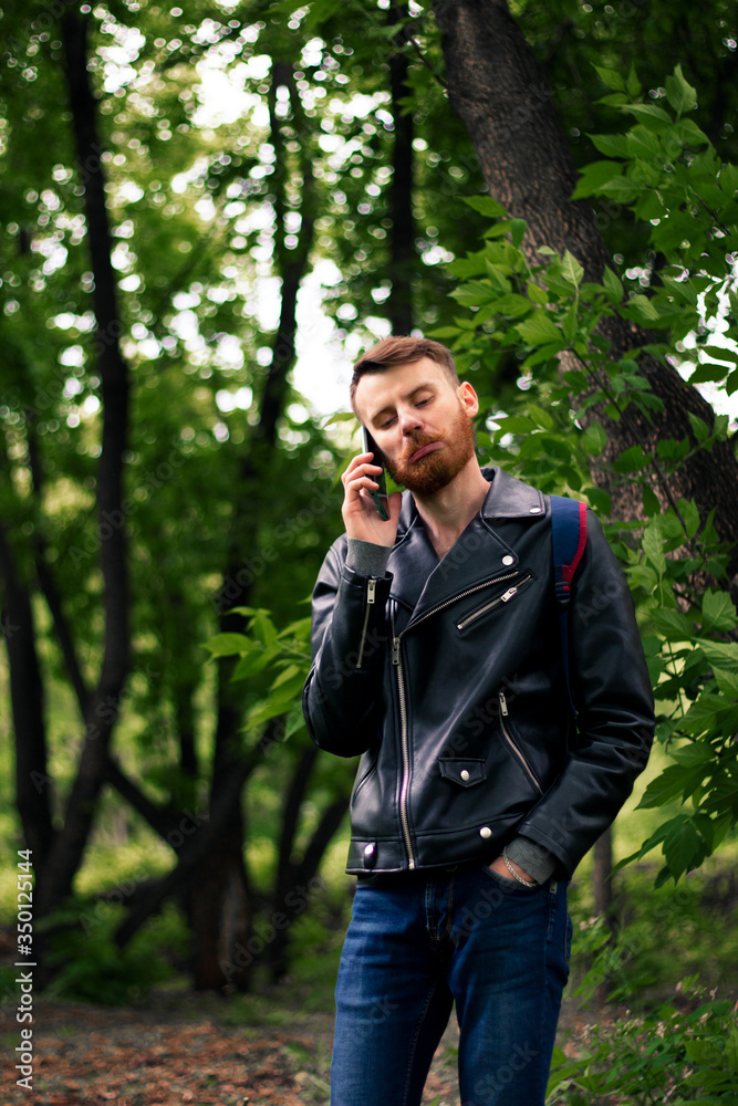 A guy with a twisted orange mustache grimaces on the phone in the park. A guy with a twisted orange mustache grimaces on the phone in the park.